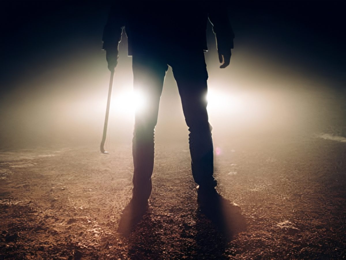 Silhouetted figure with crowbar in headlights